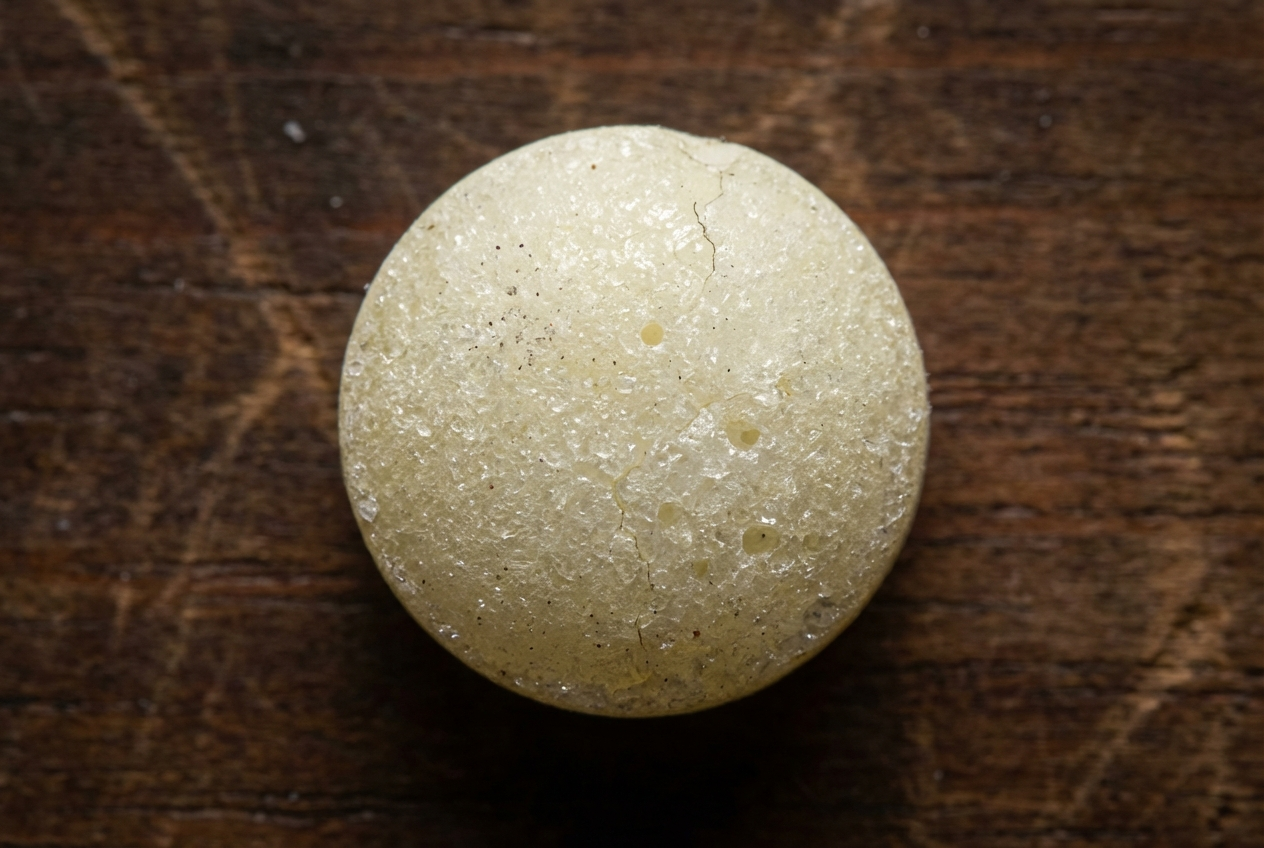 Nahaufnahme einer einzelnen, alten Mottenkugel auf einer dunklen Holzoberfläche.